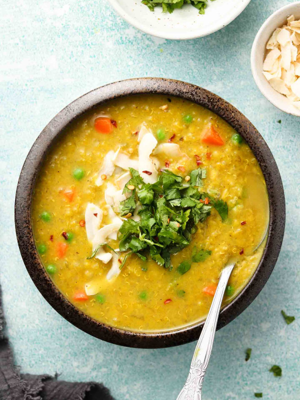 vegan lentil and quinoa curry soup with frozen vegetables in a bowl with cilantro and coconut on top
