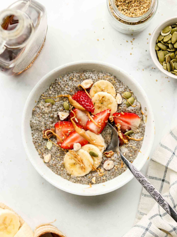 chia seed pudding in a white bowl with strawberries, bananas, nuts and peanut butter on top on a marble counter top