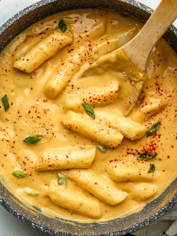 cheese tteokbokki with scallions and korean red pepper flakes in a pot with wooden spoon