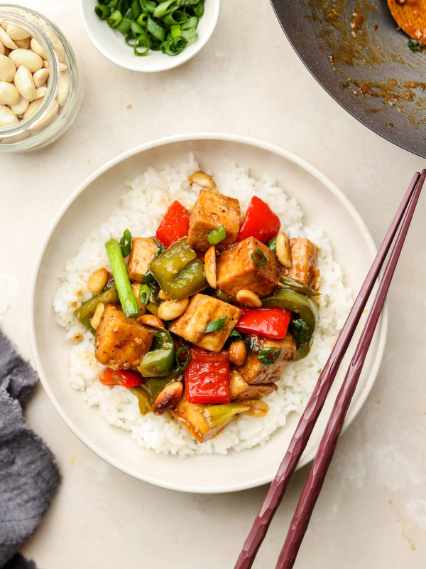 asian stir fry with bell peppers, tofu and peanuts in a bowl on top of rice