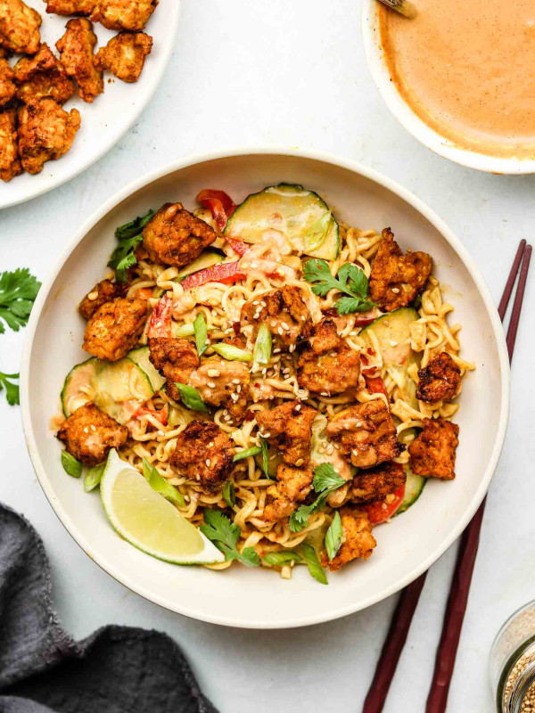 peanut noodles with baked tempeh in a white bowl with cilantro and scallions on top
