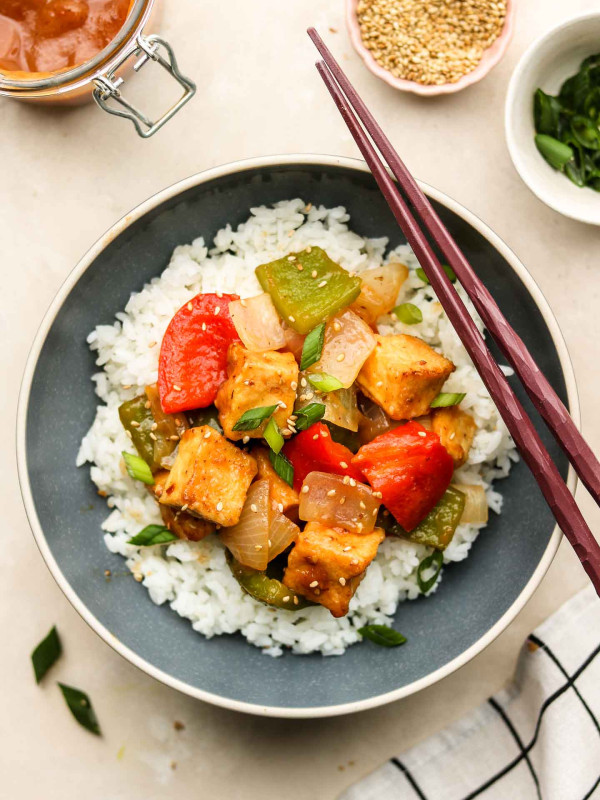 sweet and sour sauce with tofu bell pepper and onion over rice in blue bowl