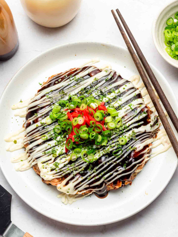 vegan okonomiyaki on a white plate with mayonnaise and scallions on top