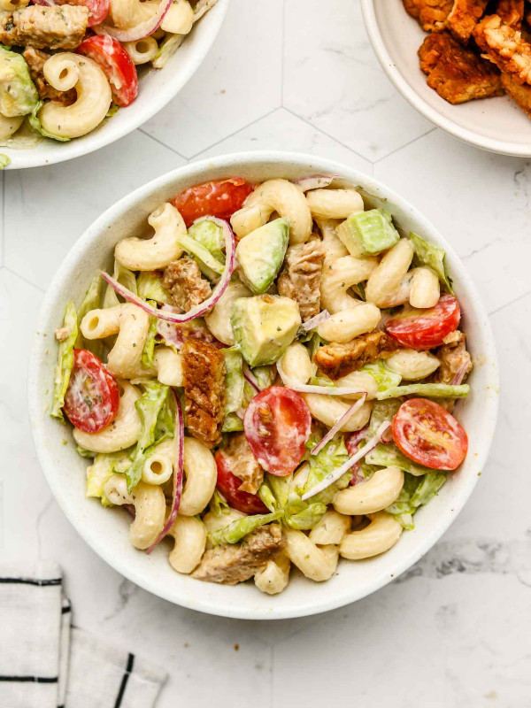blt pasta salad with tempeh bacon, tomatoes and lettuce in a white bowl with a fork in the bowl