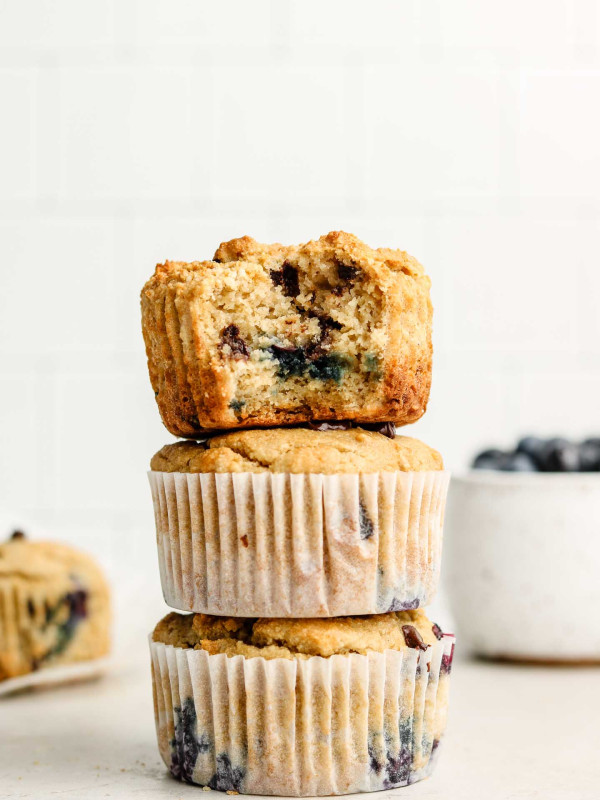 3 chocolate chip blueberry muffins stacked on each other with a bowl of blueberries in the background