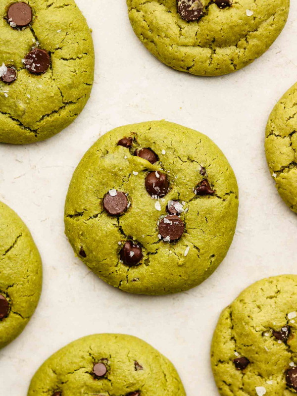 baked vegan matcha cookies with chocolate chips and flaky salt on a beige tile