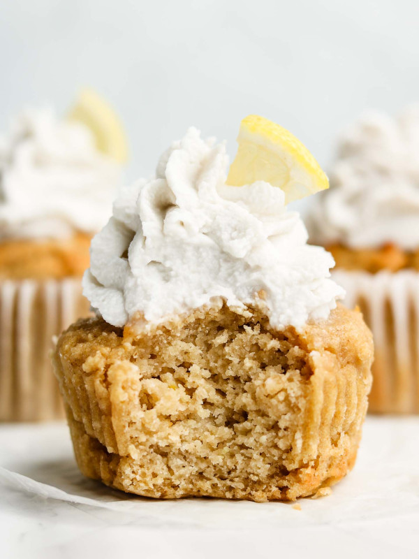 vegan lemon cupcakes with a bite taken out of it frosted with coconut cream and a slice of lemon on top