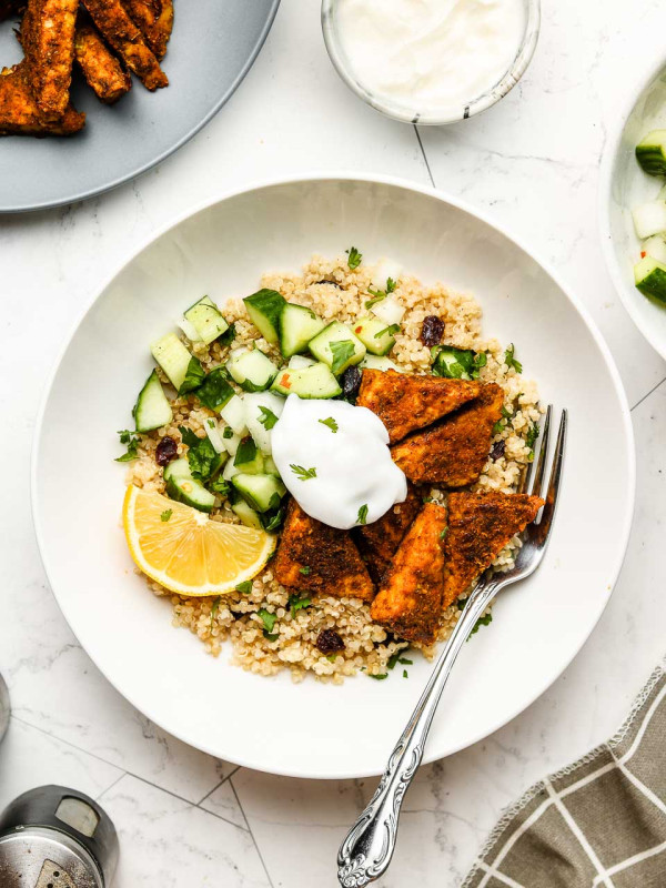 quinoa in a white bowl with tandoori tempeh, cucumber salad, yogurt and lemon