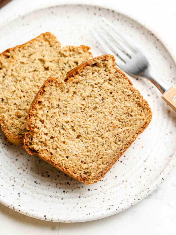 two slices of banana bread on a white speckled plate and a fork on the right side