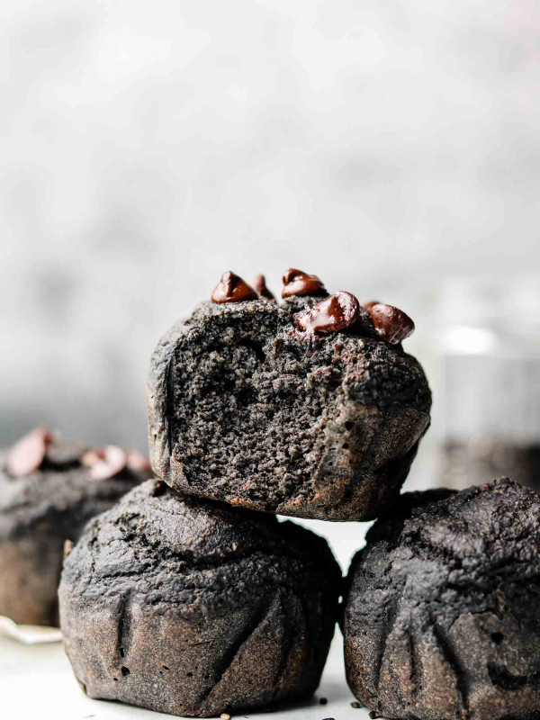 stack of black tahini banana muffins with a bite taken out of the top muffin
