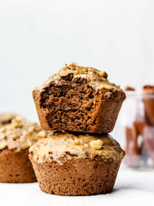two chai muffins stacked on each other with a bite taken out of the top muffin and cinnamon sticks in a jar in the back