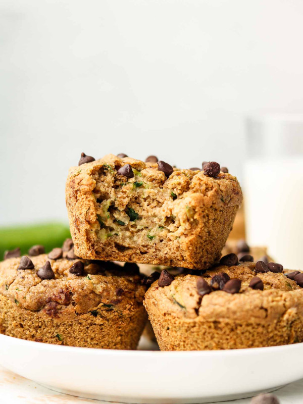 zucchini oat muffins stacked on a white plate with a bite taken out of the top one
