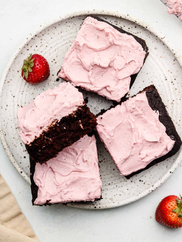 sliced of chocolate black sesame cake on a speckled white plate with strawberry whip cream on top