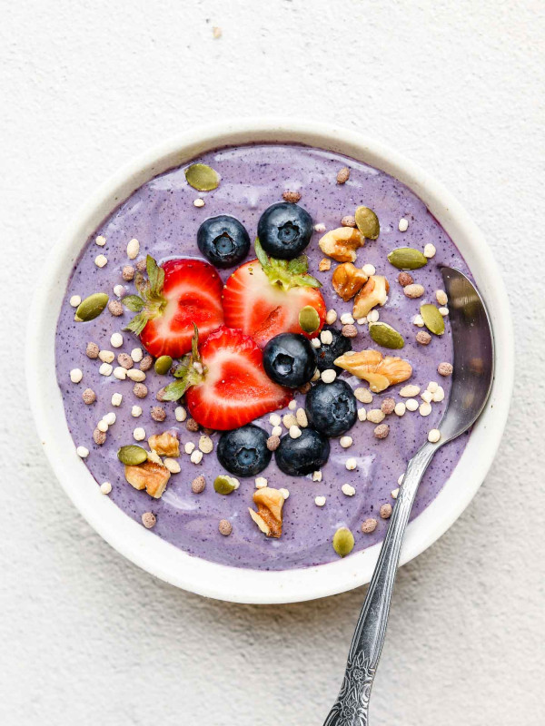 vegan blueberry yogurt in a white bowl with strawberries, blueberries, quinoa puffs, walnuts and pumpkin seeds on top