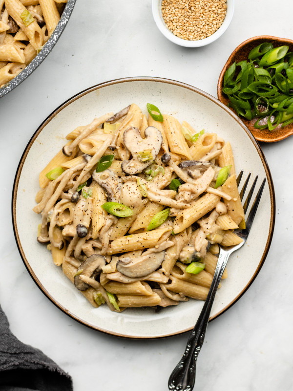 mushroom pasta on a white plate with scallions garnished on top
