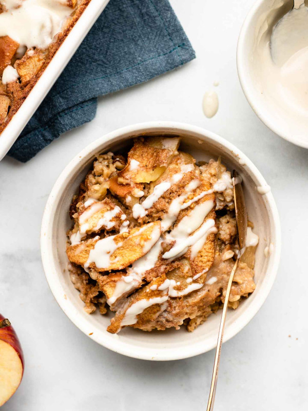 apple steel cut baked oatmeal with a drizzle of maple cashew cream in a white bowl with a rose gold spoon