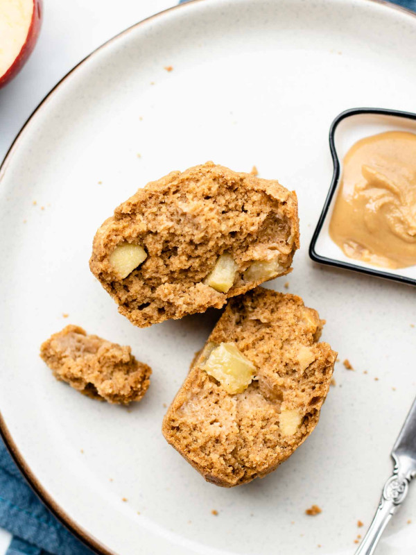 healthy chunky apple muffins on a white plate spit in half with some peanut butter beside it on a blue linen