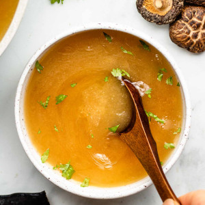 vegan bone broth in a white bowl with cilantro and spoon inside bowl