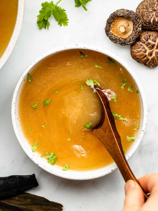vegan bone broth in a white bowl with cilantro and spoon inside bowl