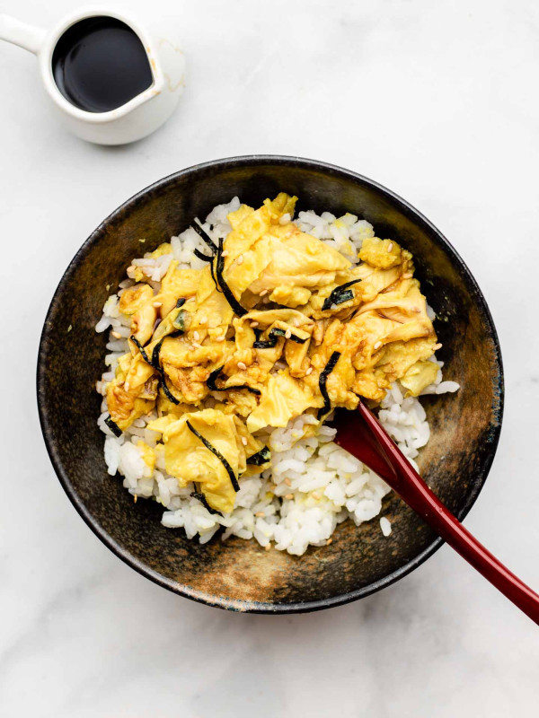 japanese scrambled eggs over a bed of rice in a bowl topped with nori and a spoon inside the bowl