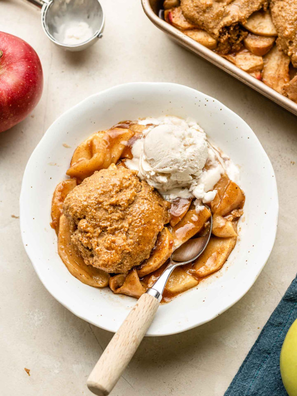 apple cobbler with biscuit topping in a white bowl with non dairy ice cream on the side