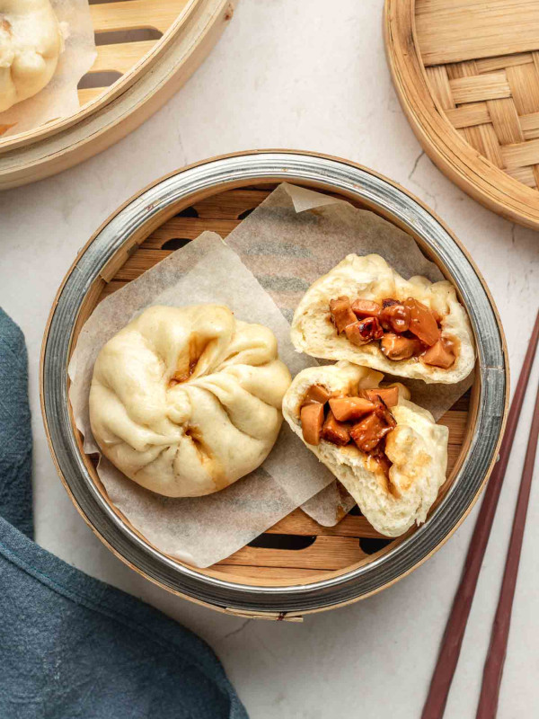 vegan char siu bao in a bamboo basket with one split in half filling showing