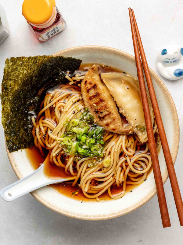 vegan shoyu ramen in a white ceramic bowl topped with green onions, nori and dumplings