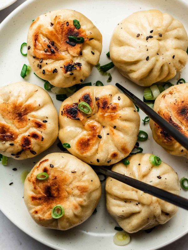 pan fried buns on a white plate with scallions on top