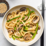 shoyu butter udon noodles with mushrooms and vegetables in a white bowl with sesame seeds