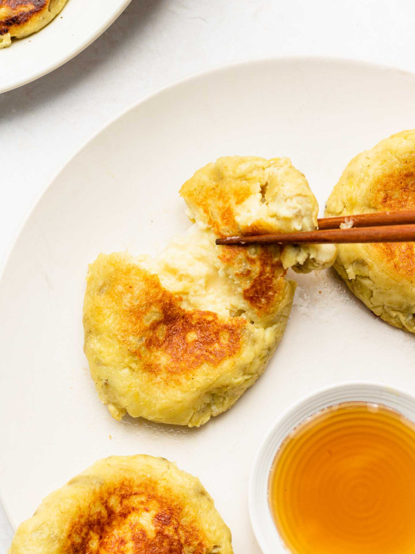 japanese sweet potato cheese mochi, stuffed with cheese and cutting it in half on a white plate served with maple syrup in a bowl