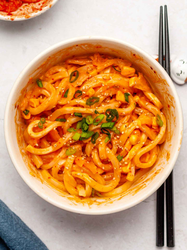 cheese and kimchi udon noodles in a white bowl with scallions on top