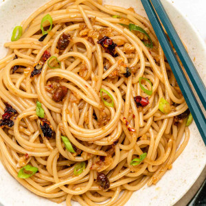 garlic noodles in a shallow white bowl with scallions and chili crisp oil