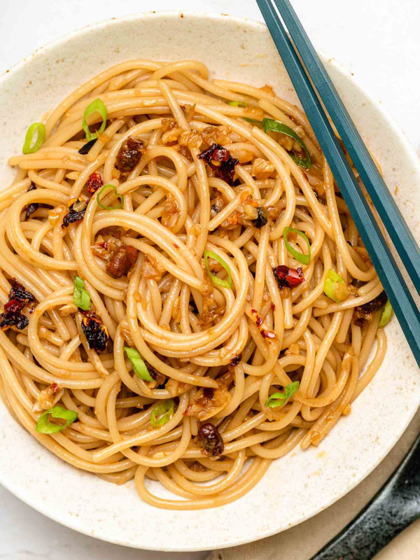 garlic noodles in a shallow white bowl with scallions and chili crisp oil