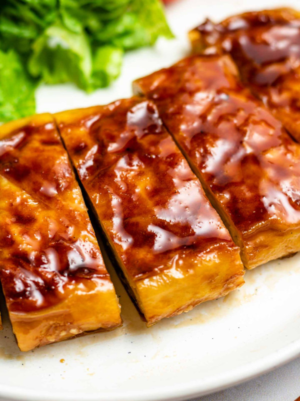vegan teriyaki tofu on a white plate sliced into bite sized pieces