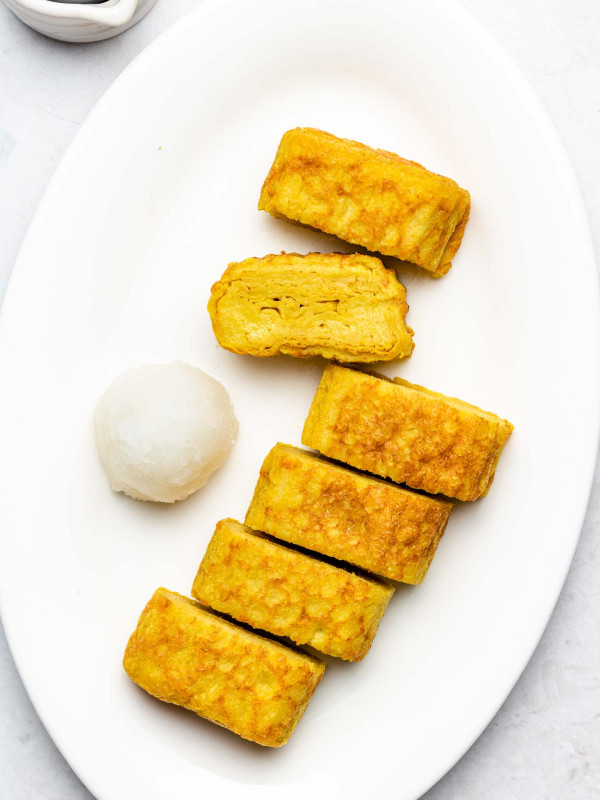 rolled omelette on a white plate with grated daikon beside it