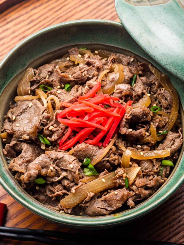 gyudon beef bowl over rice in a green donburi with pickled ginger (beni shoga) and green onions