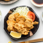 chicken tempura with cabbage, tomatoes and lemon on a black plate