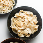 flat hand pulled noodles in a black bowl, thin noodles in a blue bowl and wide noodles in a brown bowl