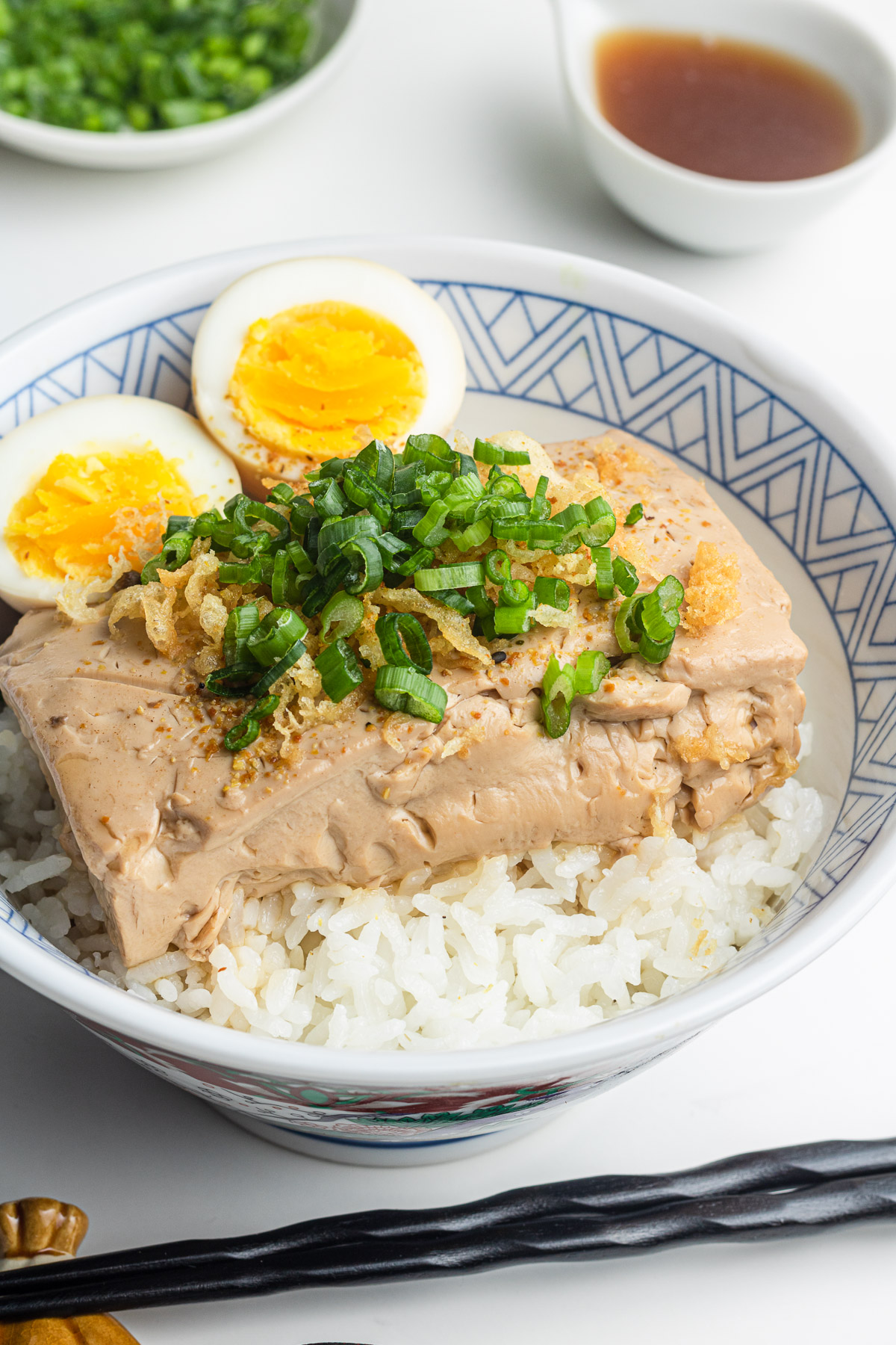 tofu and eggs over rice in a donburi bowl with scallions and tempura scraps on top