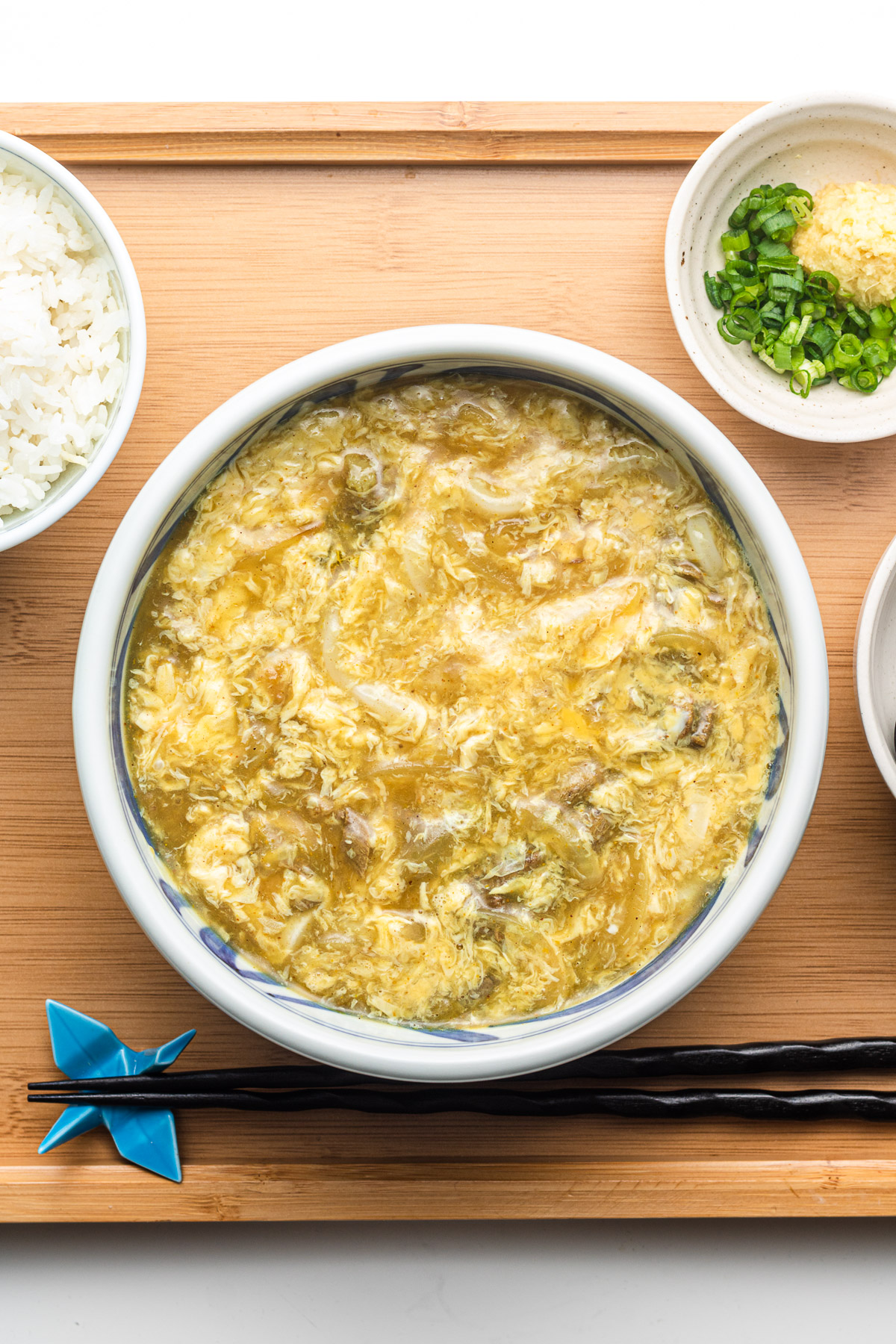 egg drop soup over udon and leftover japanese curry in a blue bowl served with ginger, scallions and rice