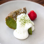matcha chocolate cake on a dessert plate with whip cream, matcha powder and strawberries