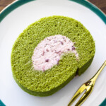Slice of matcha roll cake with adzuki cream on a dark green-rimmed plate, served with a golden fork.