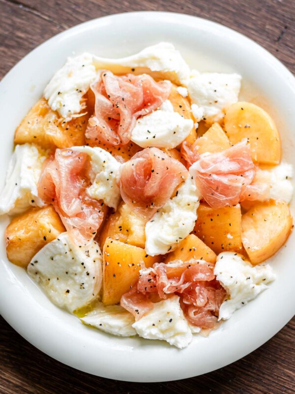 Peach, Mozzarella, and Prosciutto on a white plate with honey, olive oil and black pepper