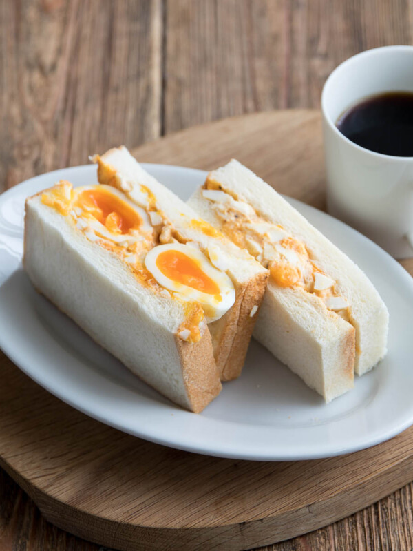 tamago sando on a white plate with black coffee beside it