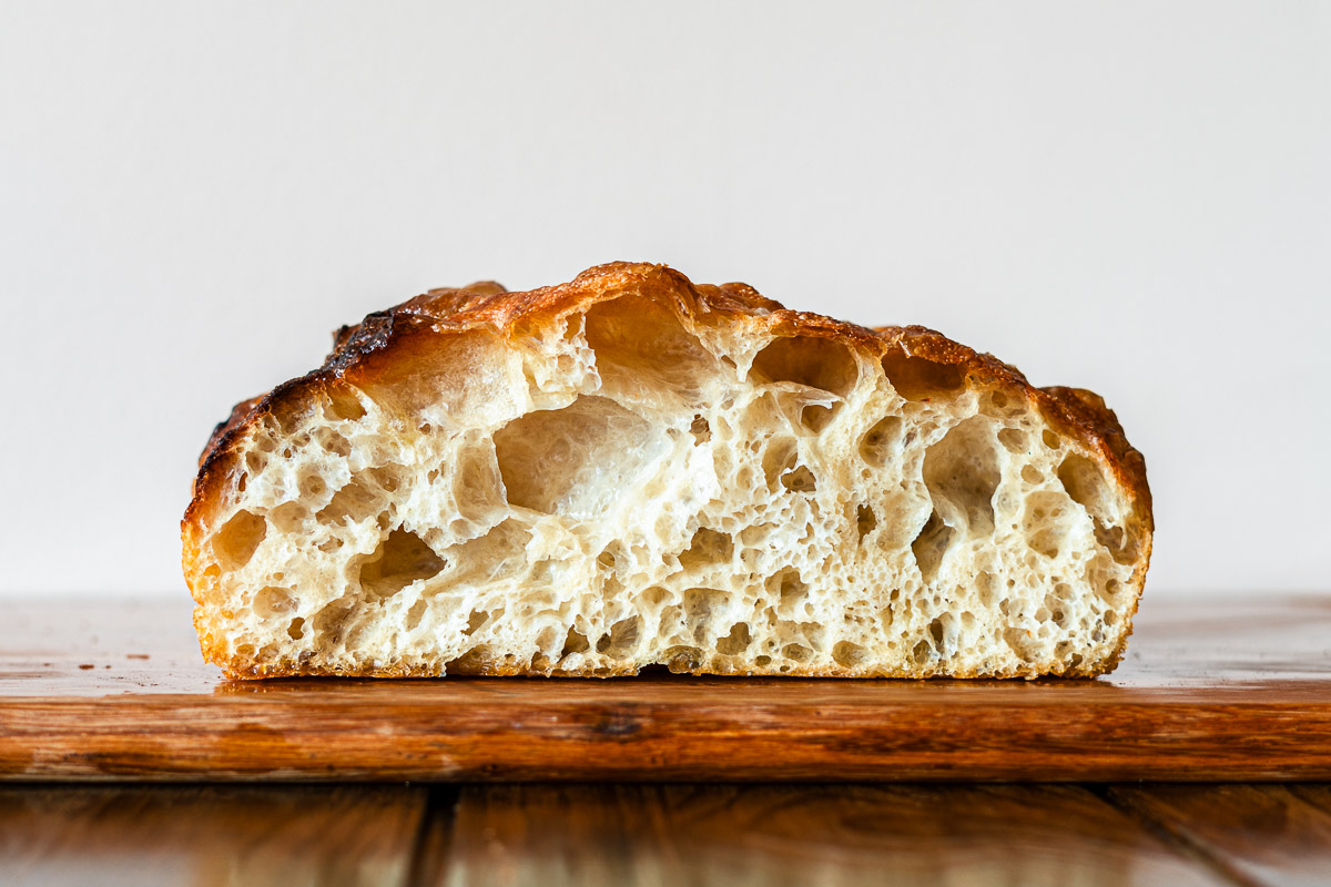 big bubbly open crumb focaccia sliced on a wooden cutting board