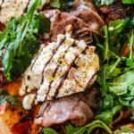 focaccia pizza with prosciutto, burrata, arugula, tomatoes, mozzarella and balsamic glaze on a cutting board