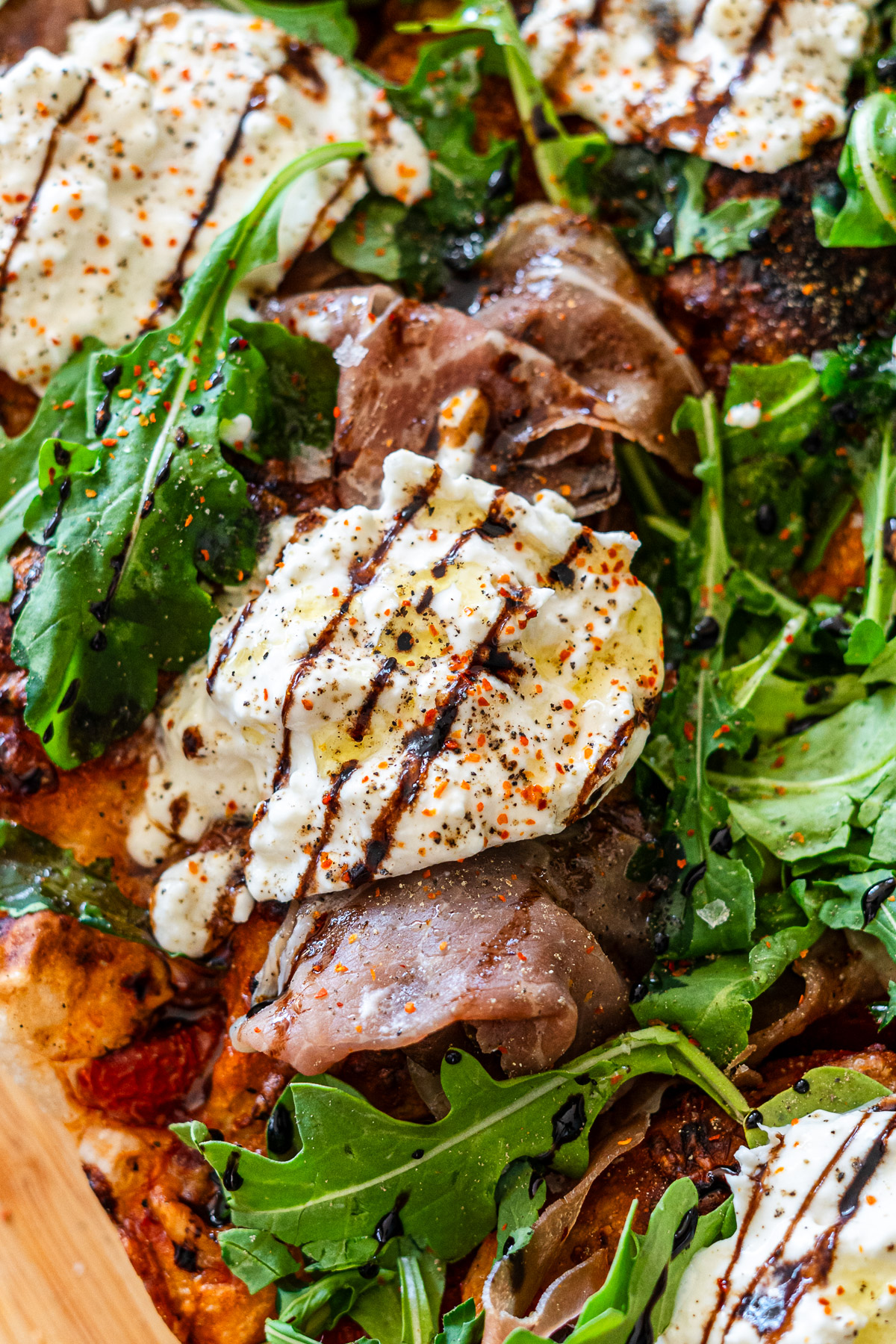 focaccia pizza with prosciutto, burrata, arugula, tomatoes, mozzarella and balsamic glaze on a cutting board