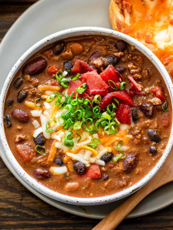 japanese curry chili in a white bowl topped with melty cheese, scallion and pickles
