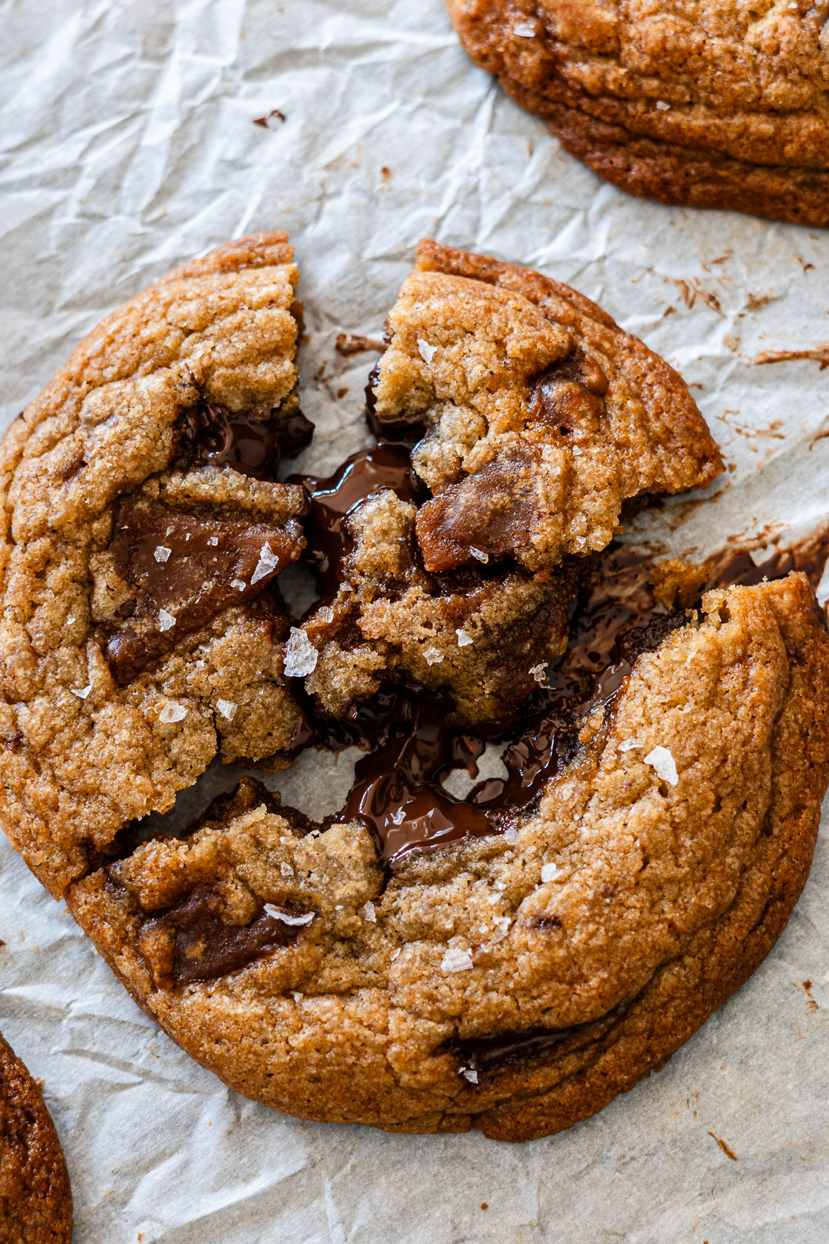 brown butter melty gooey chocolate chunk cookies broken on a parchment paper