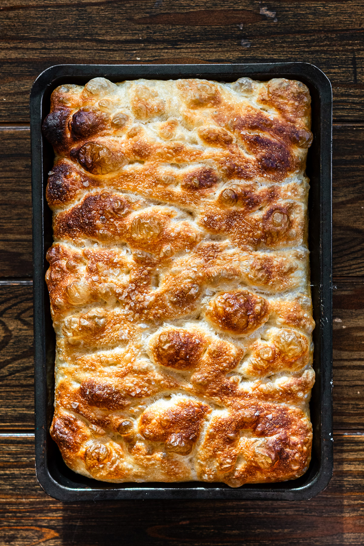 crispy golden butter focaccia in a pan with flaky salt on top